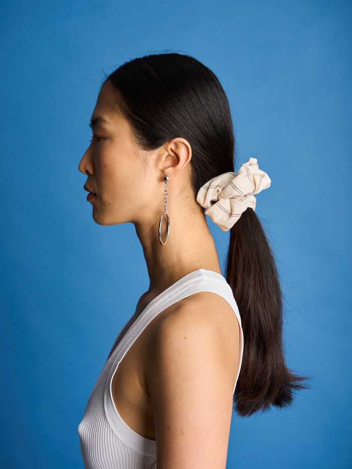 The Lucie Marquis 'Susie Scrunchie' is a stylish oversized hair scrunchie made from leftover fabric scraps. The scrunchie is 7cm wide and designed to wrap around twice. It features a brand label stitched flat on one side. The scrunchie effortlessly elevates any outfit. A great travel accessory, sustainably made.