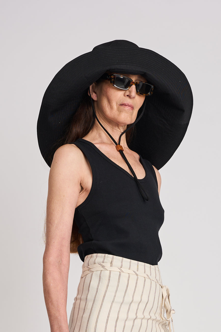 The Lucie Marquis 'Dylan Sunhat' is a wide brimmed sun hat made from high quality cotton twill with heavy topstitching and a wooden block cord end. Inspired by the iconic spirit of Bob Dylan and the bold essence of Georgia O'Keeffe, the sun hat embodies timeless style with a subtle nod to the 70s and a touch of cowboy charm. Perfect for shielding from the sun, it's the ideal accessory for your travel adventures.