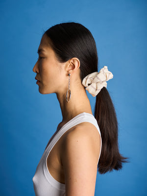 The Lucie Marquis 'Susie Scrunchie' is a stylish oversized hair scrunchie made from leftover fabric scraps. The scrunchie is 7cm wide and designed to wrap around twice. It features a brand label stitched flat on one side. The scrunchie effortlessly elevates any outfit. A great travel accessory, sustainably made.